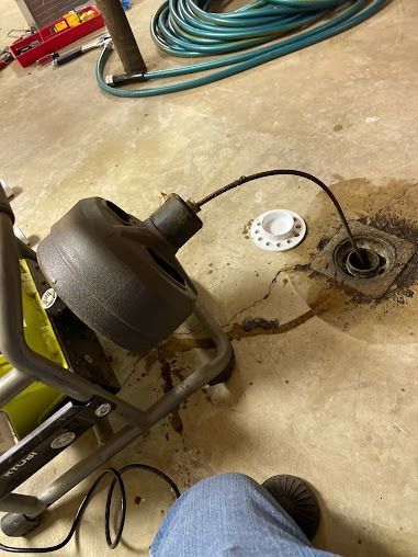 A person is using a drain cleaner to clean a drain in a basement.