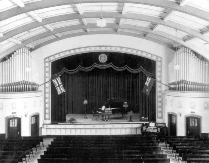 A historic black and white photo of Darke Hall auditorium with a piano on stage