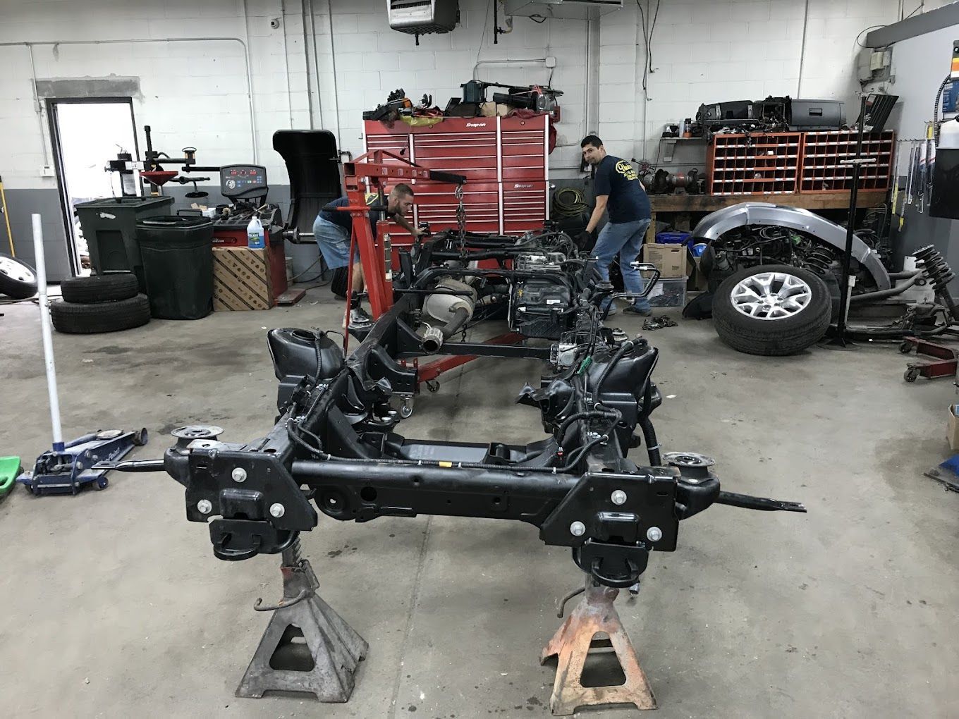 Two men are working on a car frame in a garage.