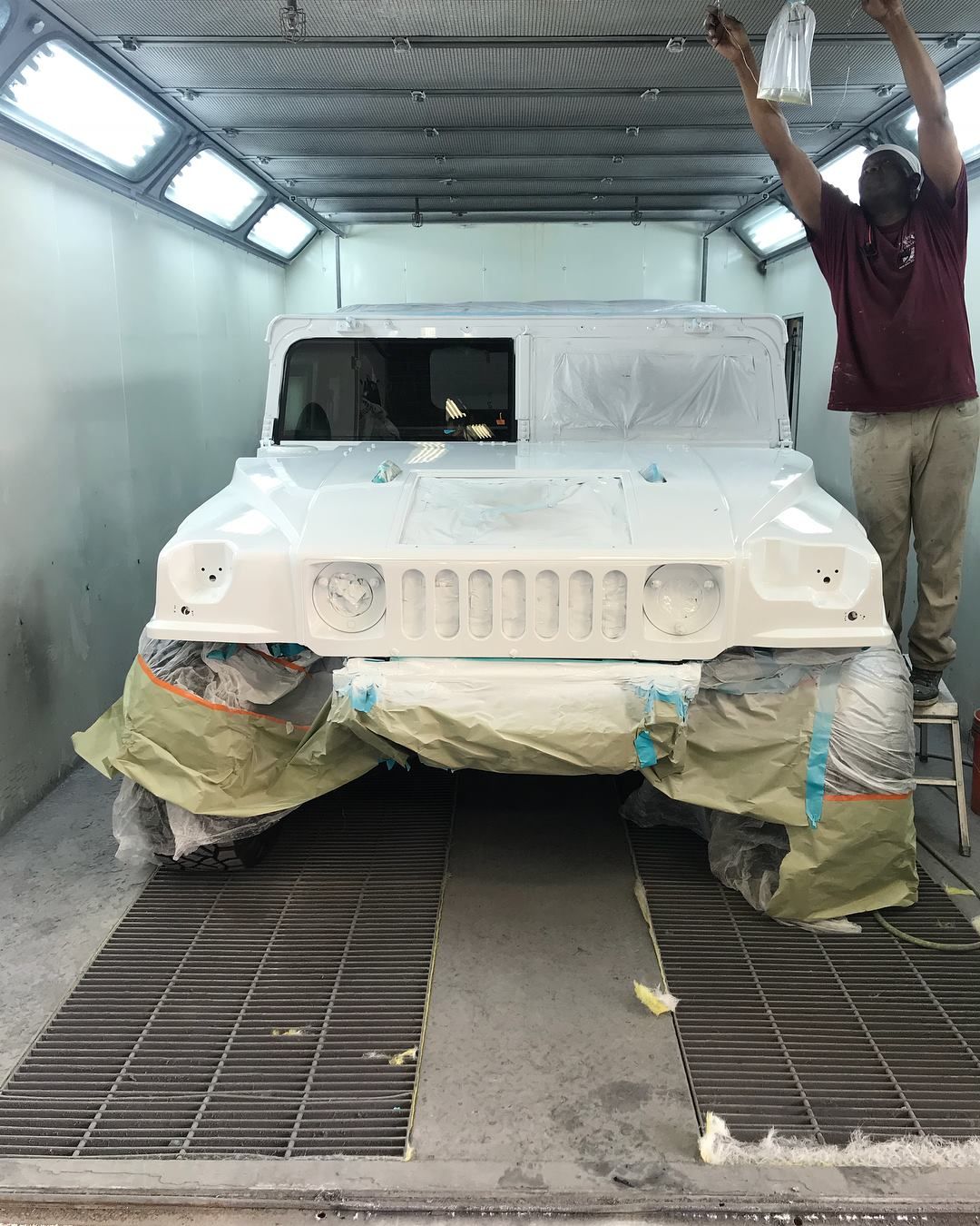 A man is painting a white vehicle in a paint booth.