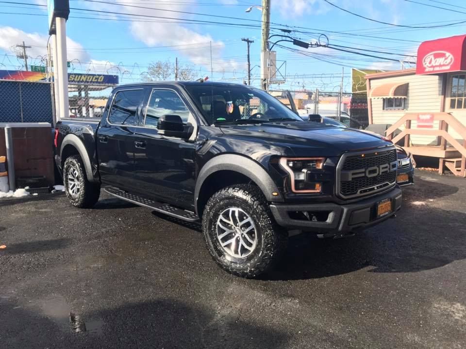 A black ford raptor truck is parked in a parking lot.