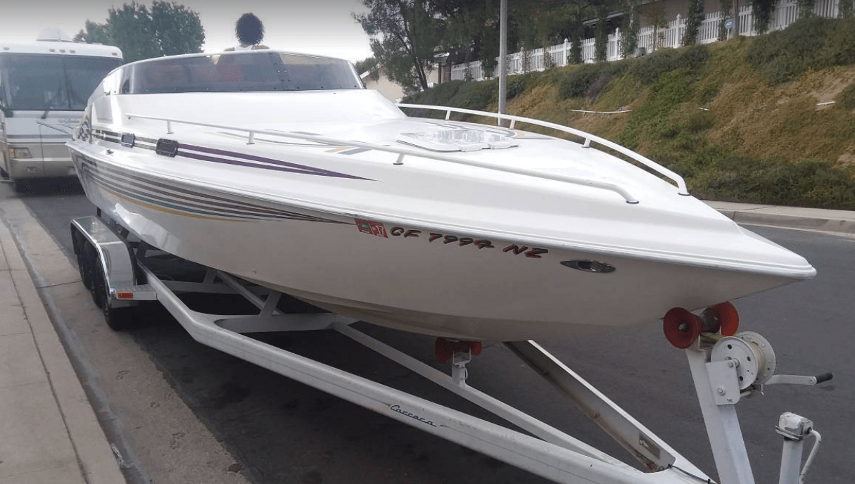 A white boat is on a trailer parked on the side of the road.