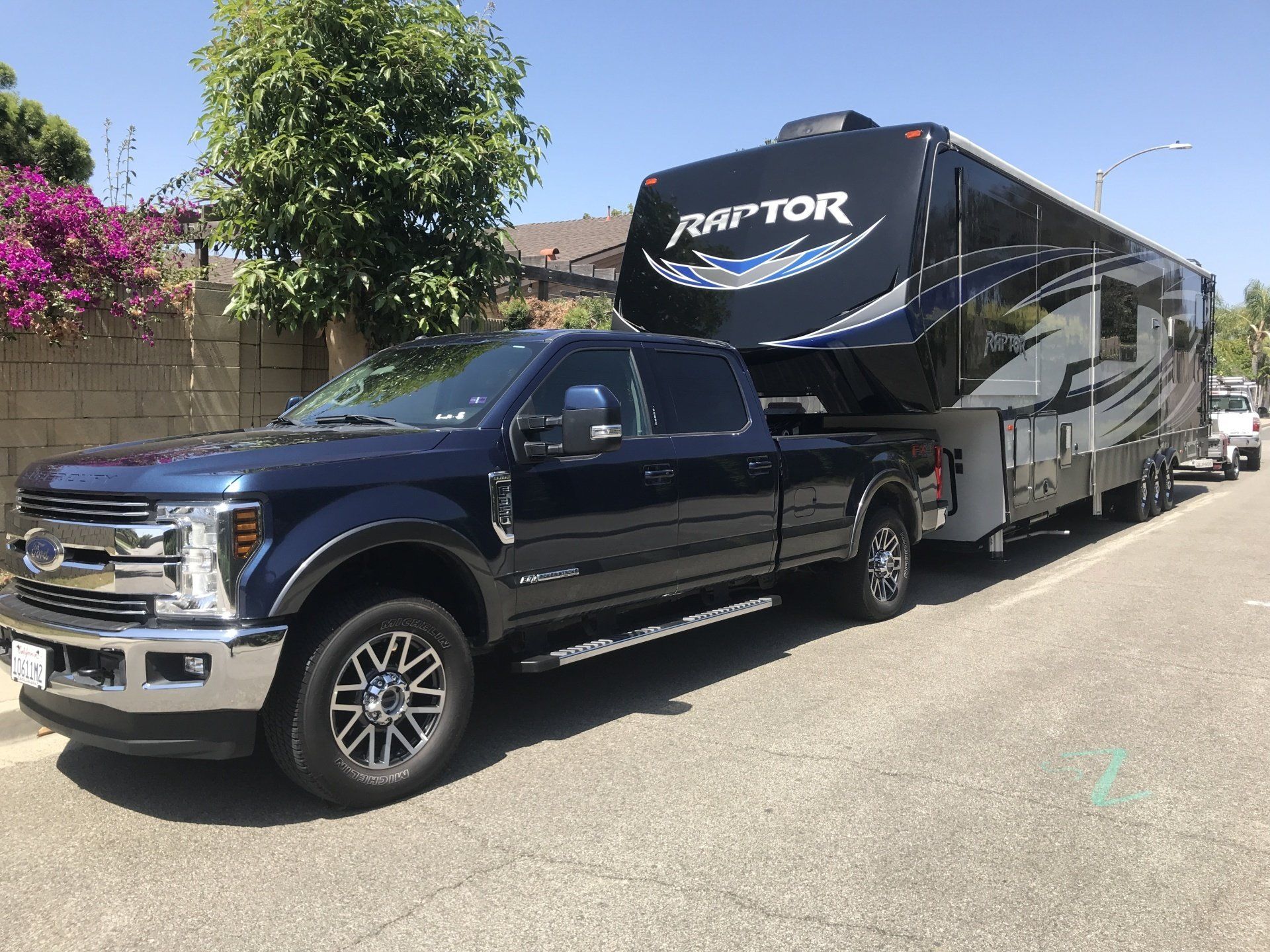A blue truck is towing a rv down a street.