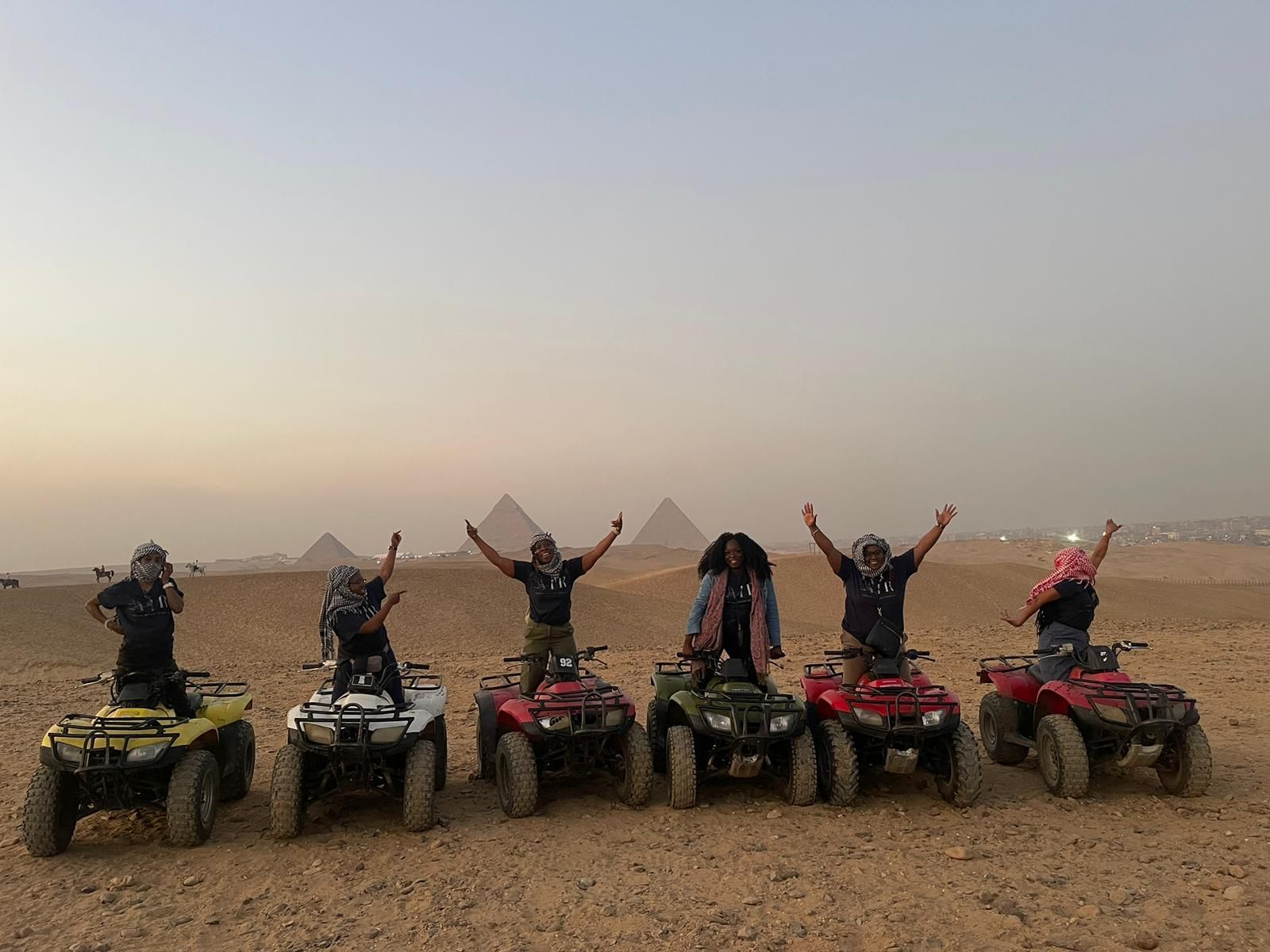 A group of people are riding atvs in the desert in front of the pyramids.