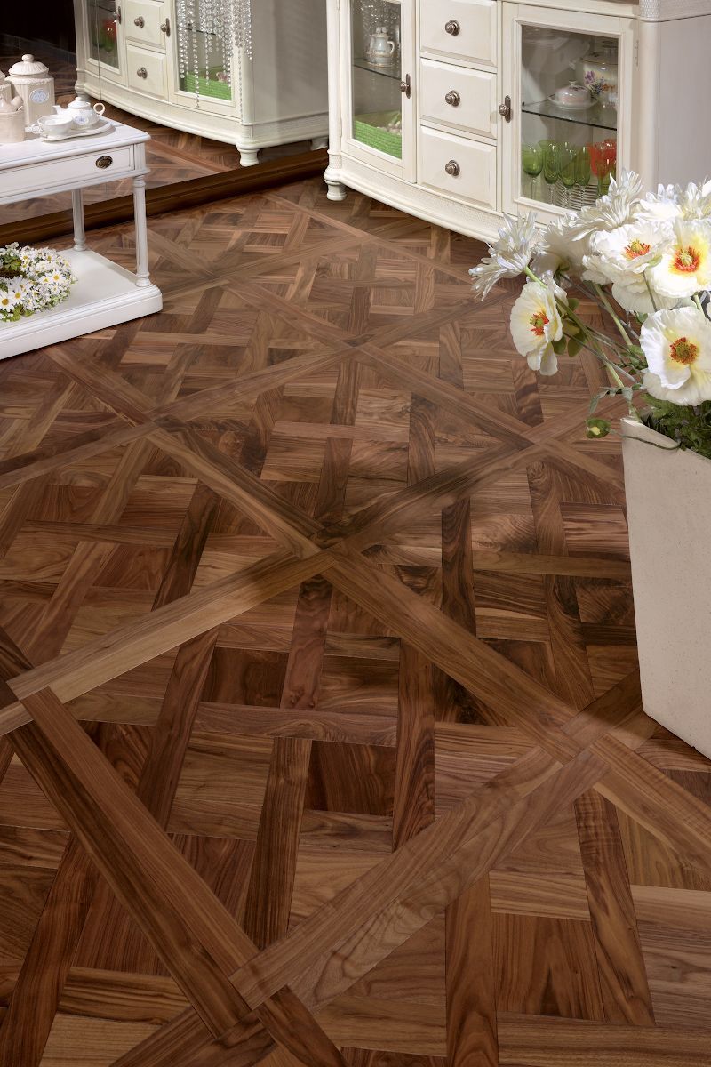 Wooden floor with patterned squares and lines, next to white furniture and a flower arrangement.