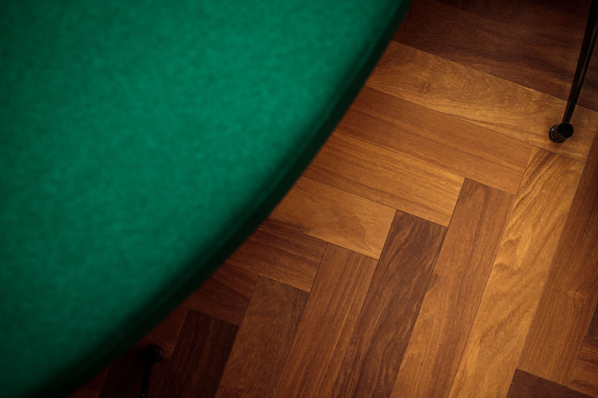 Green felt tabletop edge beside a parquet wood floor.