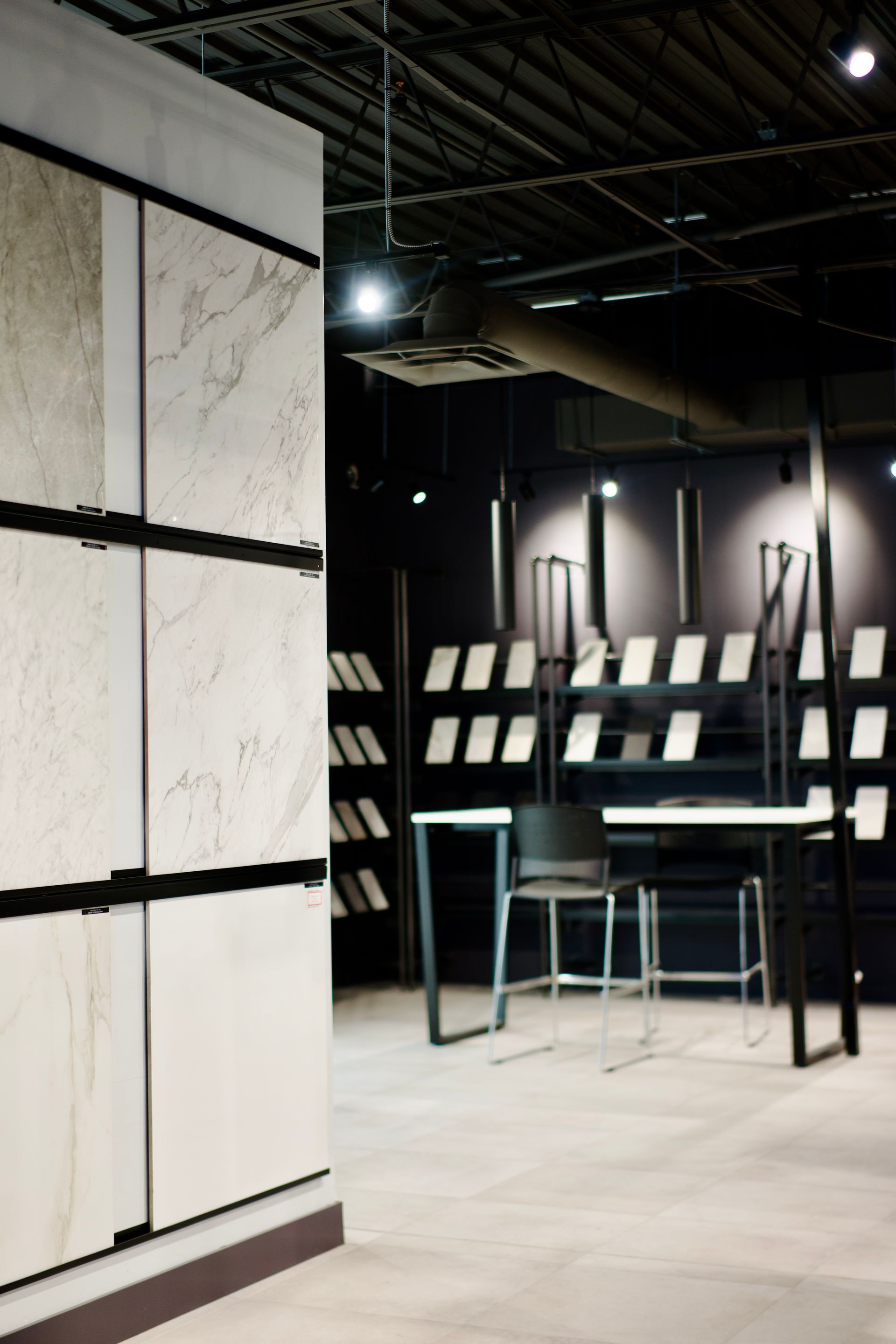 Intérieur d'une salle d'exposition, présentant des échantillons de pierre sur un mur et des étagères, avec une petite table et des tabourets.
