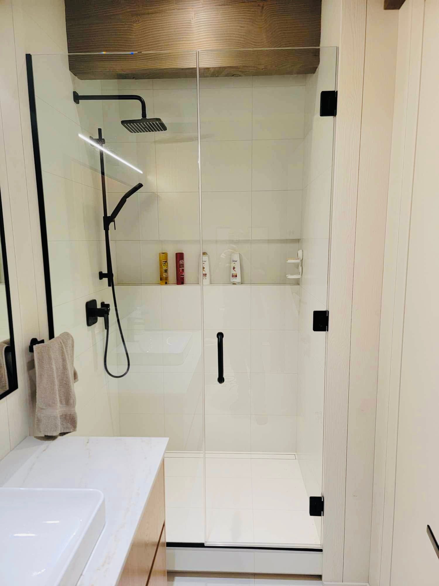 Modern bathroom with glass shower enclosure, white tiles, and black fixtures.