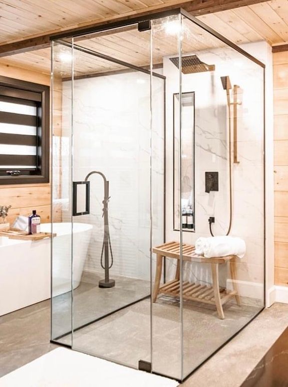 Modern bathroom with glass shower, soaking tub, wooden accents, and gold fixtures.