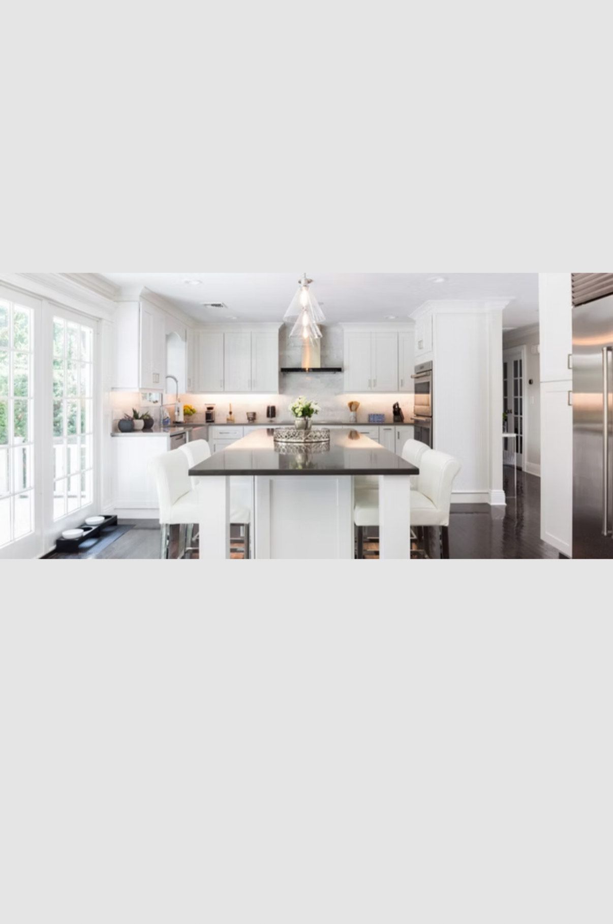 Modern white kitchen with island, stainless steel appliances, and dark flooring.