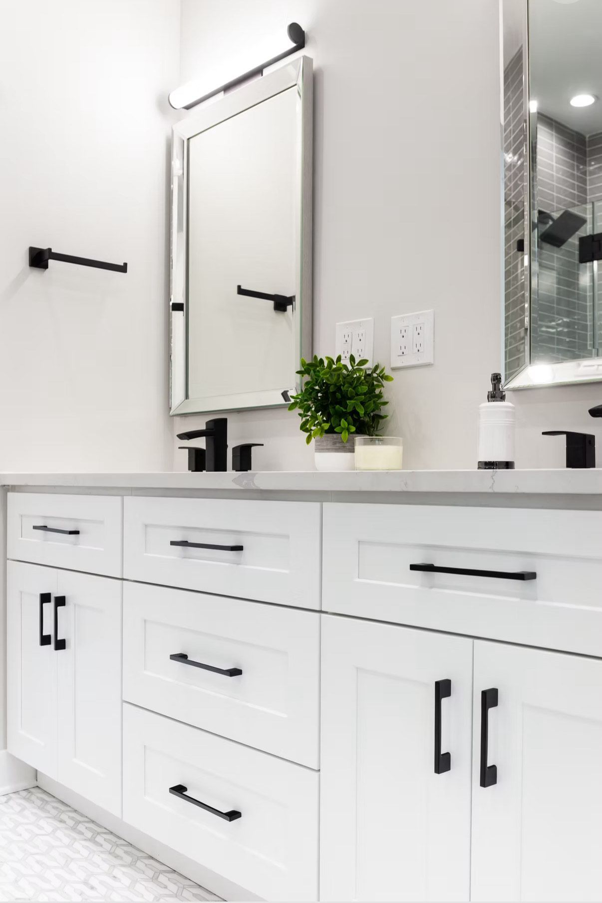 White bathroom vanity with black hardware, mirror, and faucet. Small potted plant on countertop.