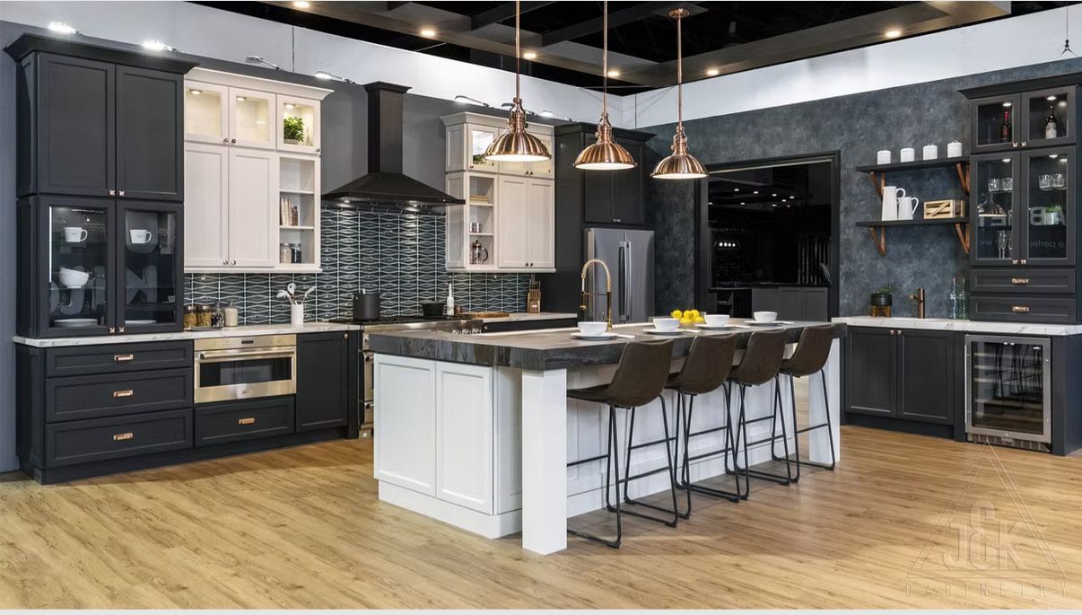 Cuisine moderne avec placards foncés et blancs, îlot central avec tabourets et suspensions lumineuses en cuivre.