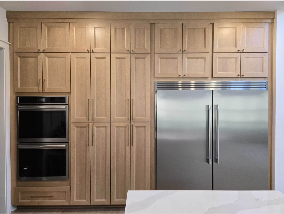 Cuisine avec placards en bois clair, réfrigérateur en acier inoxydable et fours doubles encastrés.