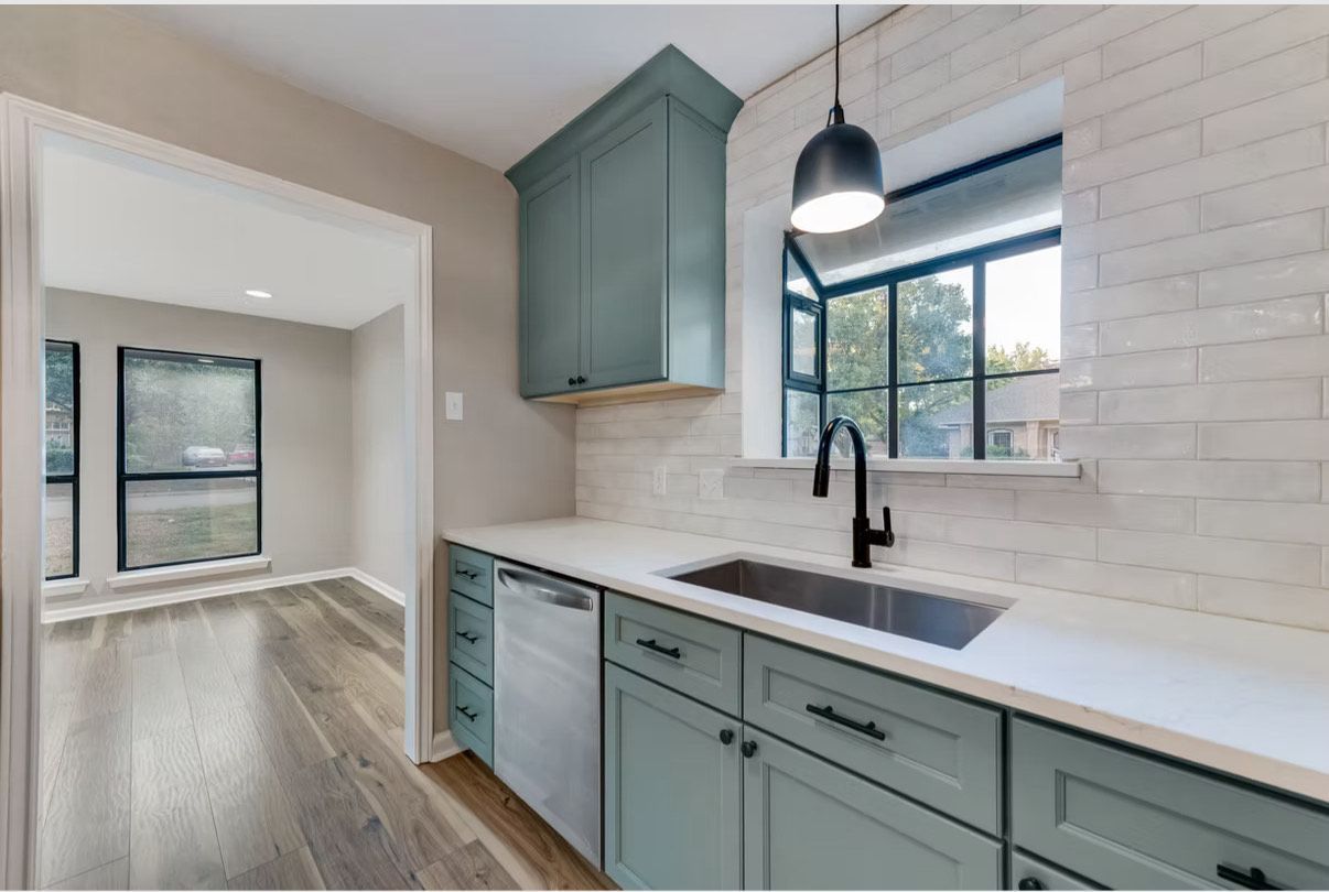 Cuisine avec placards bleus, comptoirs blancs, crédence en briques et robinet noir.