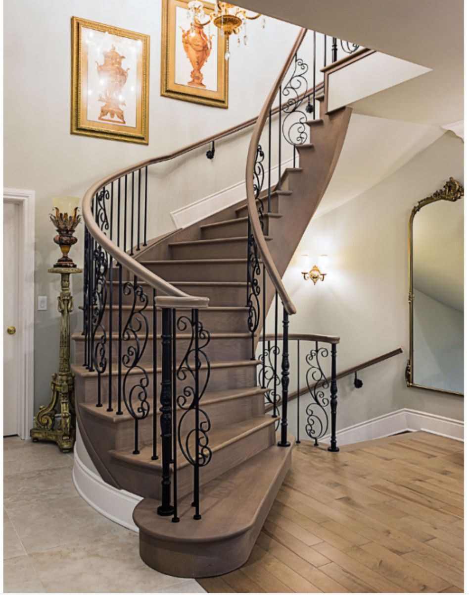 Elegant curved staircase with black iron railing, wooden steps, and a gold-framed mirror.