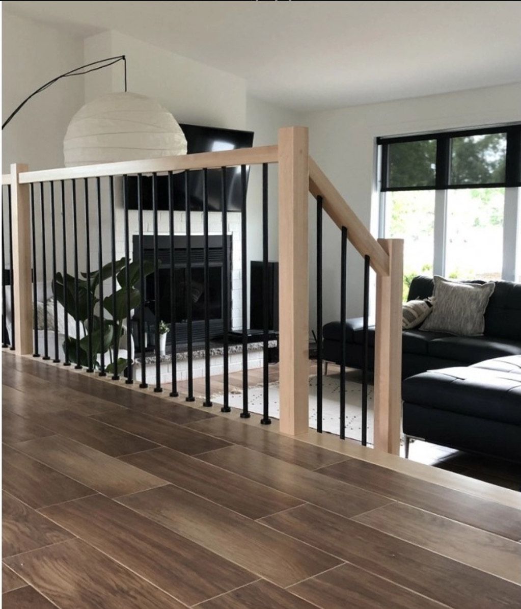 Wooden floor with a railing and black spindles, leading to a living room with a fireplace and couch.
