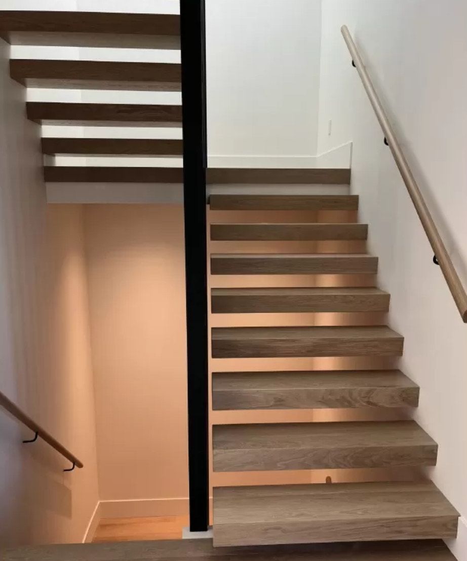 Escalier en bois avec des accents de cuivre et une poutre de soutien noire, à l'intérieur d'une maison bien éclairée.