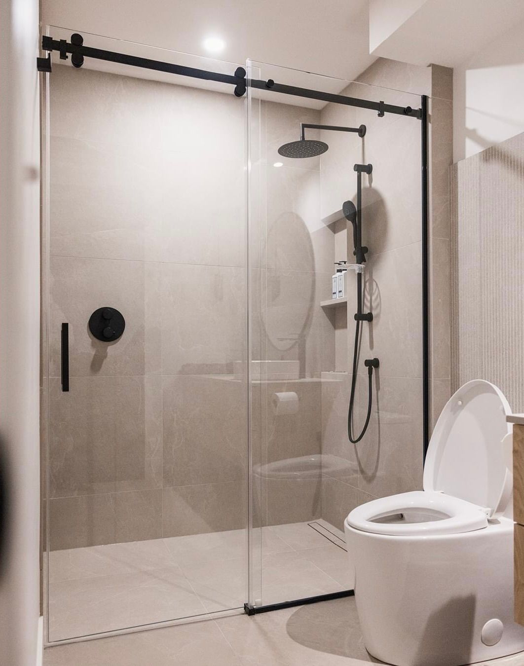 Modern bathroom with glass shower, black fixtures, and toilet.