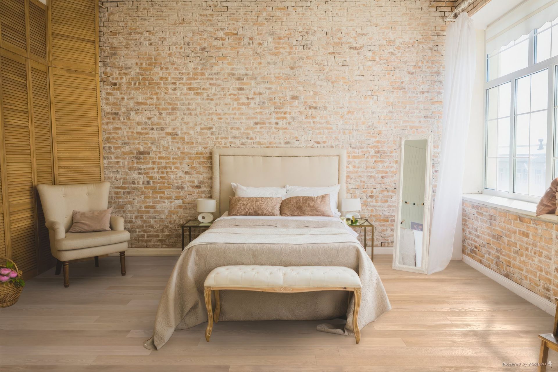 Une chambre avec murs en briques apparentes et parquet clair. Un lit avec une tête de lit beige et une literie neutre, un banc au pied du lit et une chaise.