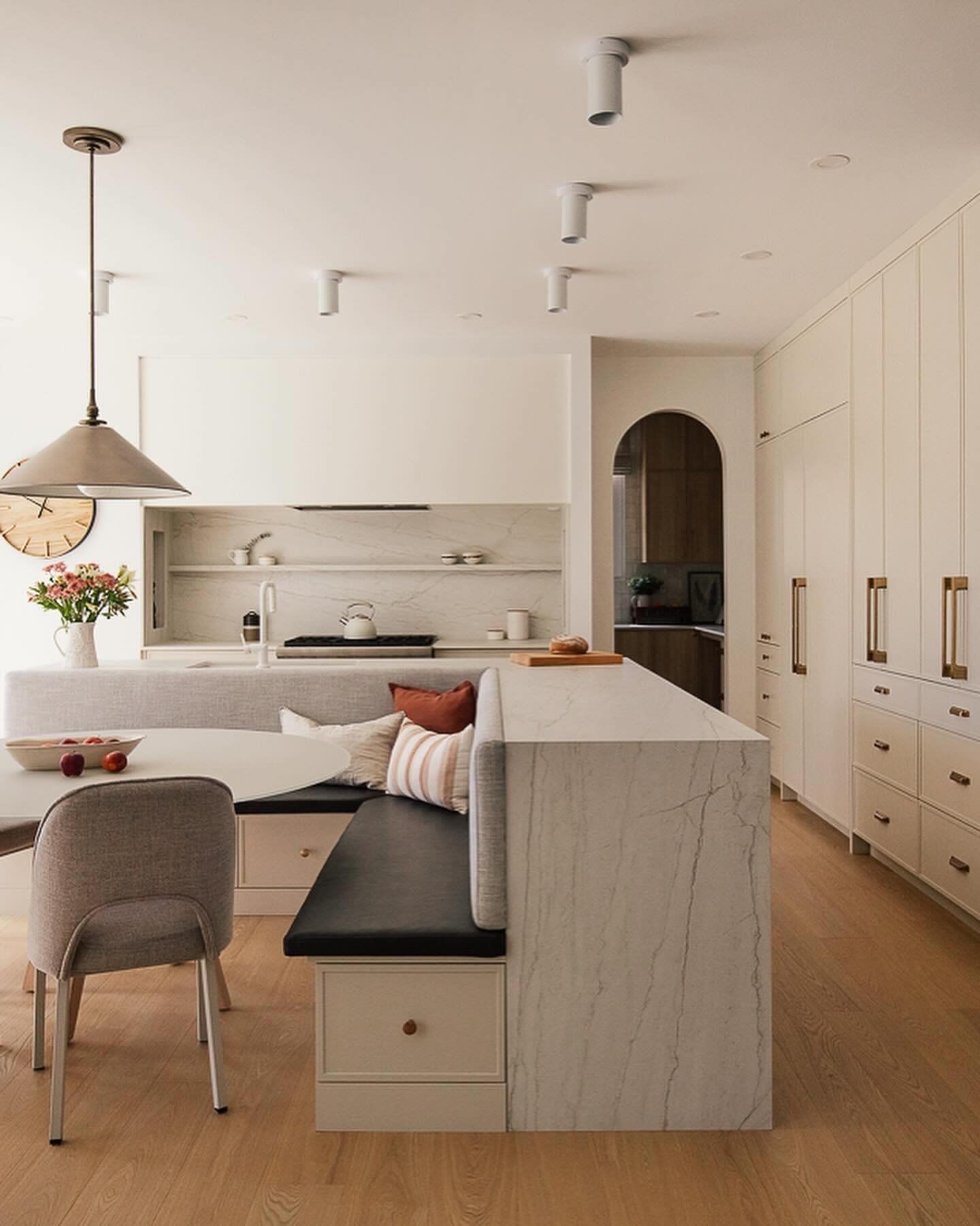 Cuisine lumineuse et aérée avec sièges intégrés, îlot en marbre et armoires hautes dans des tons neutres.