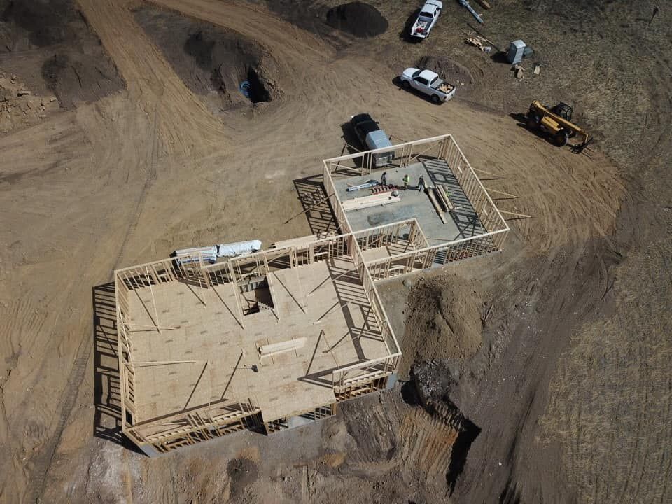 Aerial view of a house under construction. Wooden frames sit on a dirt lot with construction vehicles.