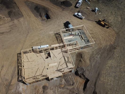 Aerial view of a house under construction. Wooden frames sit on a dirt lot with construction vehicles.