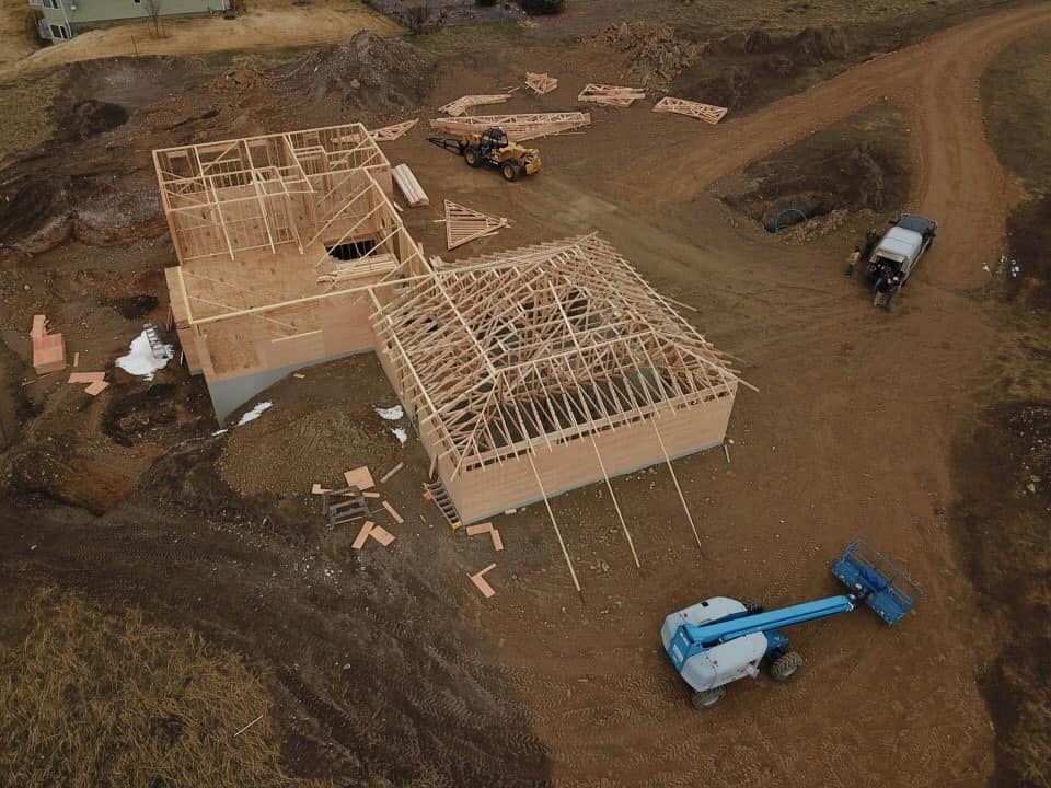 Construction site with two wooden framed buildings, lumber, heavy equipment, and a blue lift.