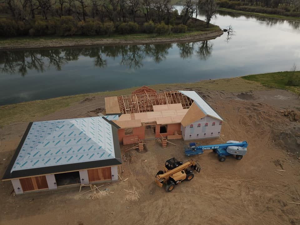 Construction site by a river: a house and garage under construction, with machinery.