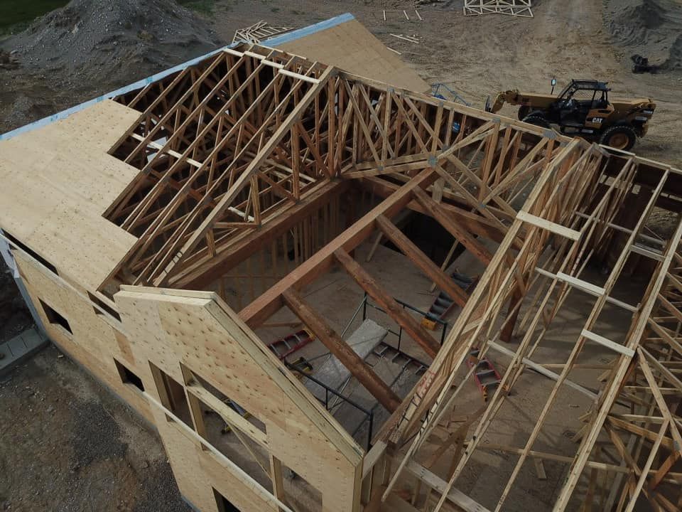 Construction site with wooden roof trusses being installed on a two-story building. A small truck is present.