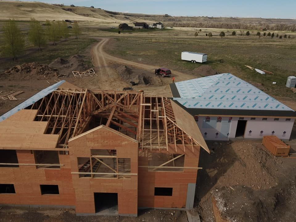 Construction site: partially built house with exposed framing, another building, dirt road in rural setting.