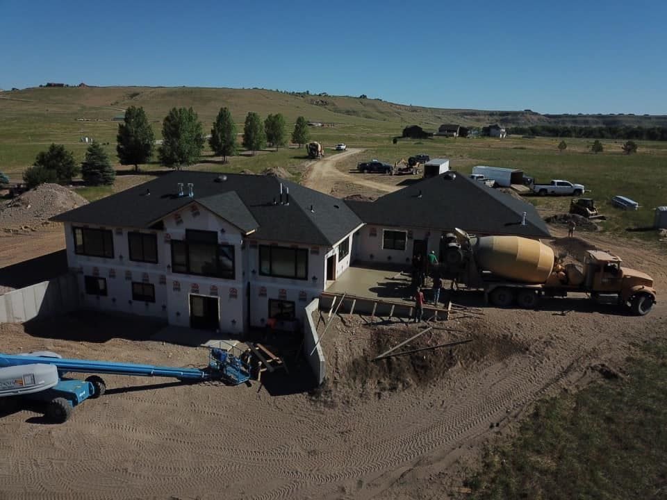 House under construction, with a cement truck pouring concrete on a sunny day.