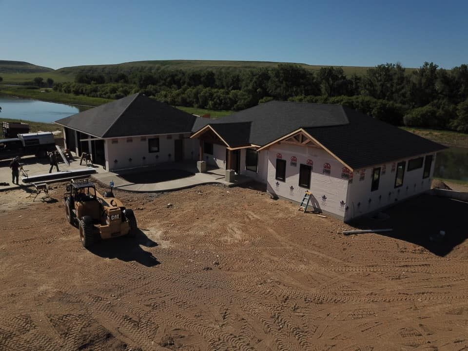 A partially-built house with a black roof on a construction site next to a pond.
