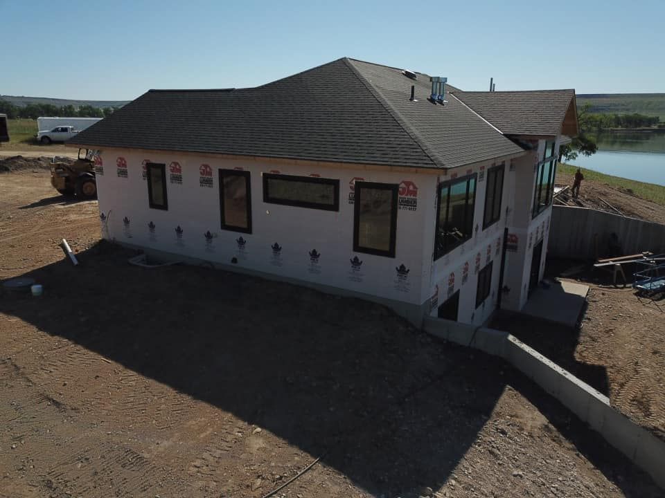Newly constructed two-story house, light-pink siding, dark roof, and black framed windows, on a hillside overlooking water.