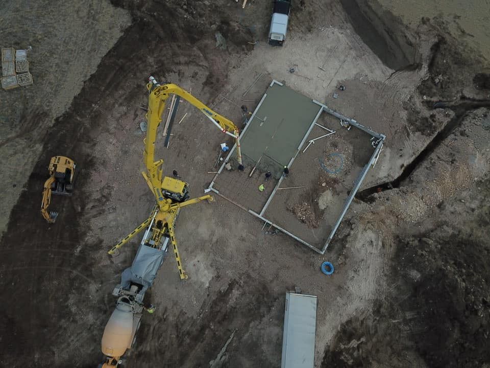 Aerial view of a construction site with a concrete pump pouring cement into a foundation.