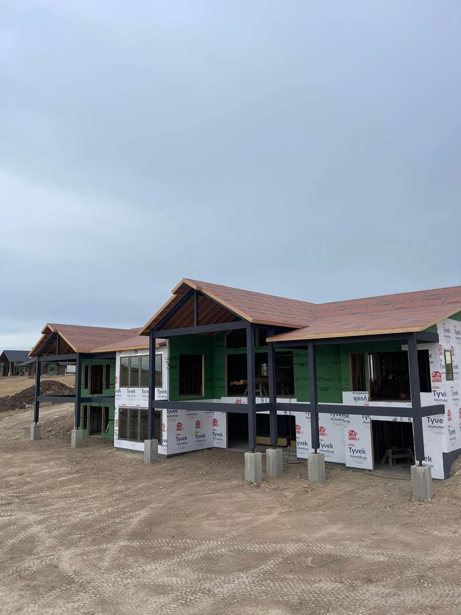 Buildings under construction with exposed framing and green sheathing; dirt lot, overcast sky.