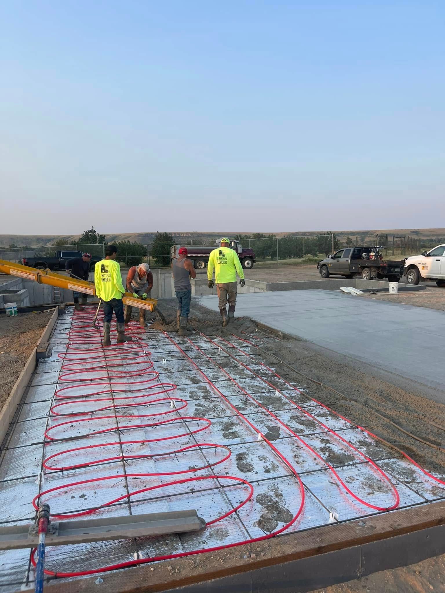 Workers installing red tubing for radiant heat in concrete.