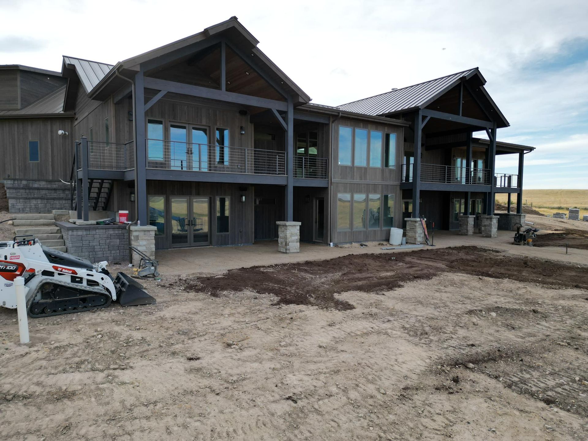 Rustic wooden house under construction; brown siding, steel roof. Dirt yard with a small tractor.