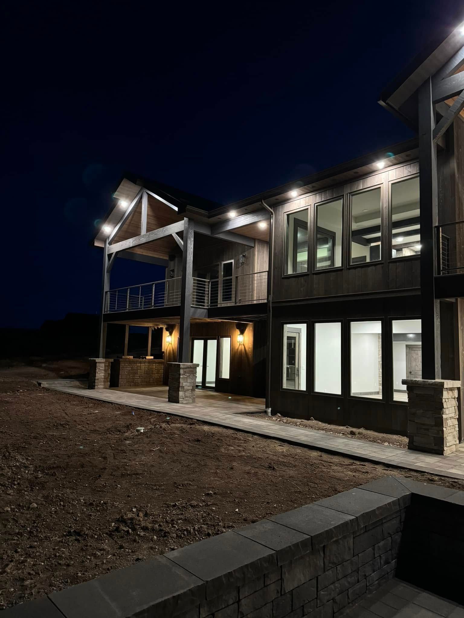 Two-story modern house at night with outdoor lighting. Large windows, dark siding, open porch.