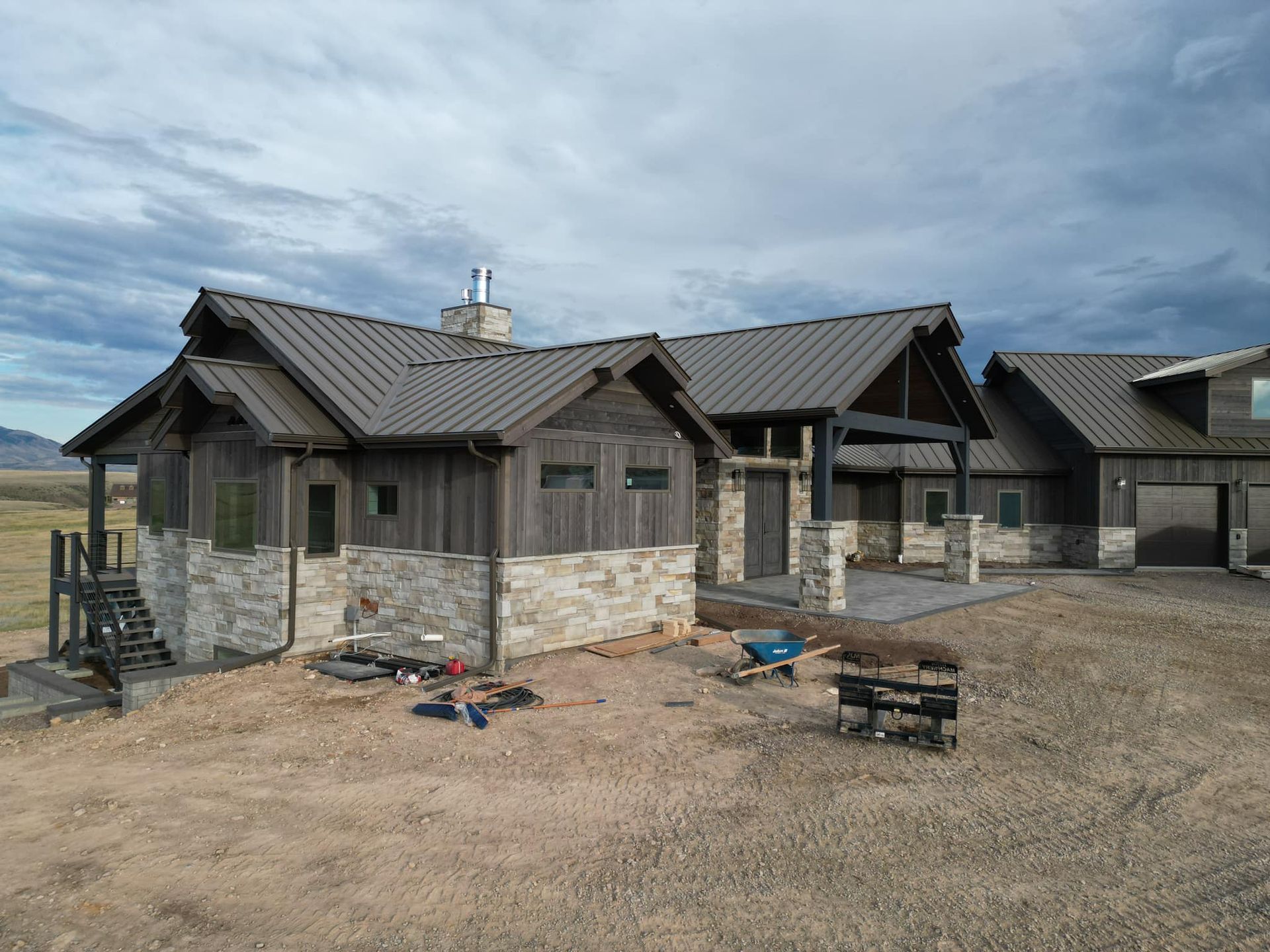 Rustic home with stone and wood exterior, metal roof, set in a dry, open landscape.