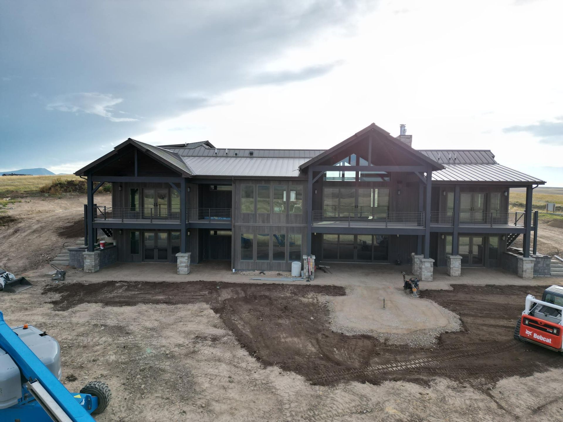 Large modern house under construction with dark gray exterior. Cloudy sky.