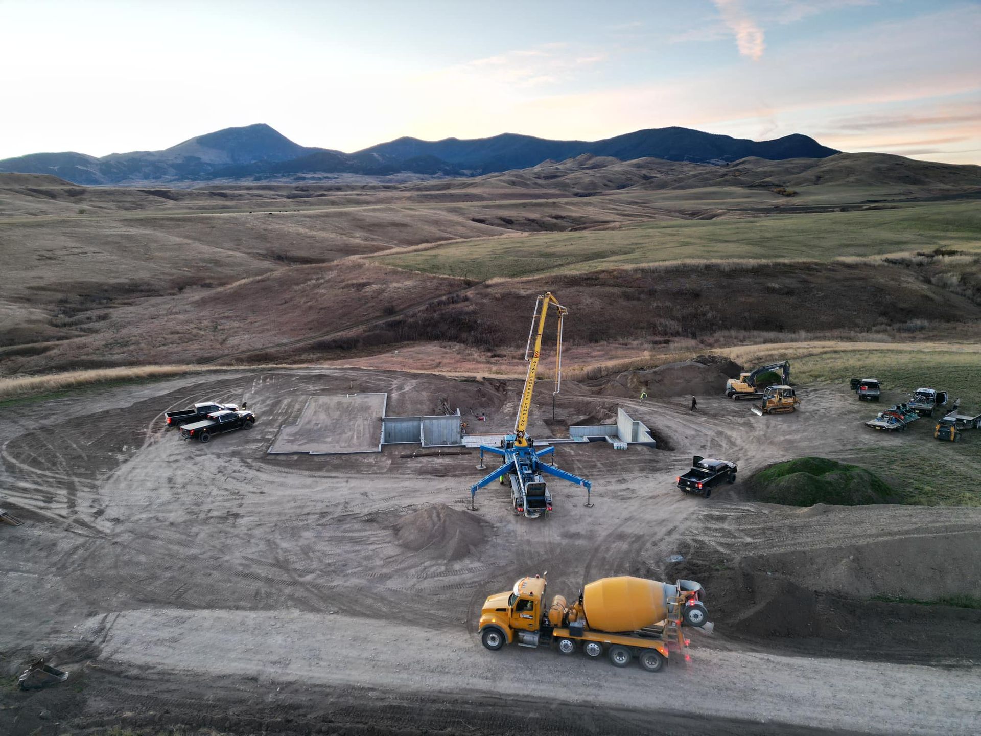 Construction site with concrete truck pouring concrete; a pump truck is also in use. Mountain backdrop.
