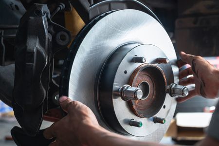 Hands installing a new brake rotor on a vehicle, workshop setting.