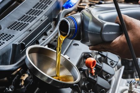 Pouring fresh oil from a container into a car engine, using a funnel.