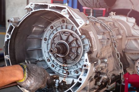 Close-up of a disassembled car transmission. A gloved hand is visible, suggesting repair in a shop.