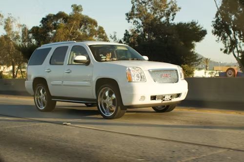 A white GMC Yukon SUV driving on a highway with chrome rims during the daytime.