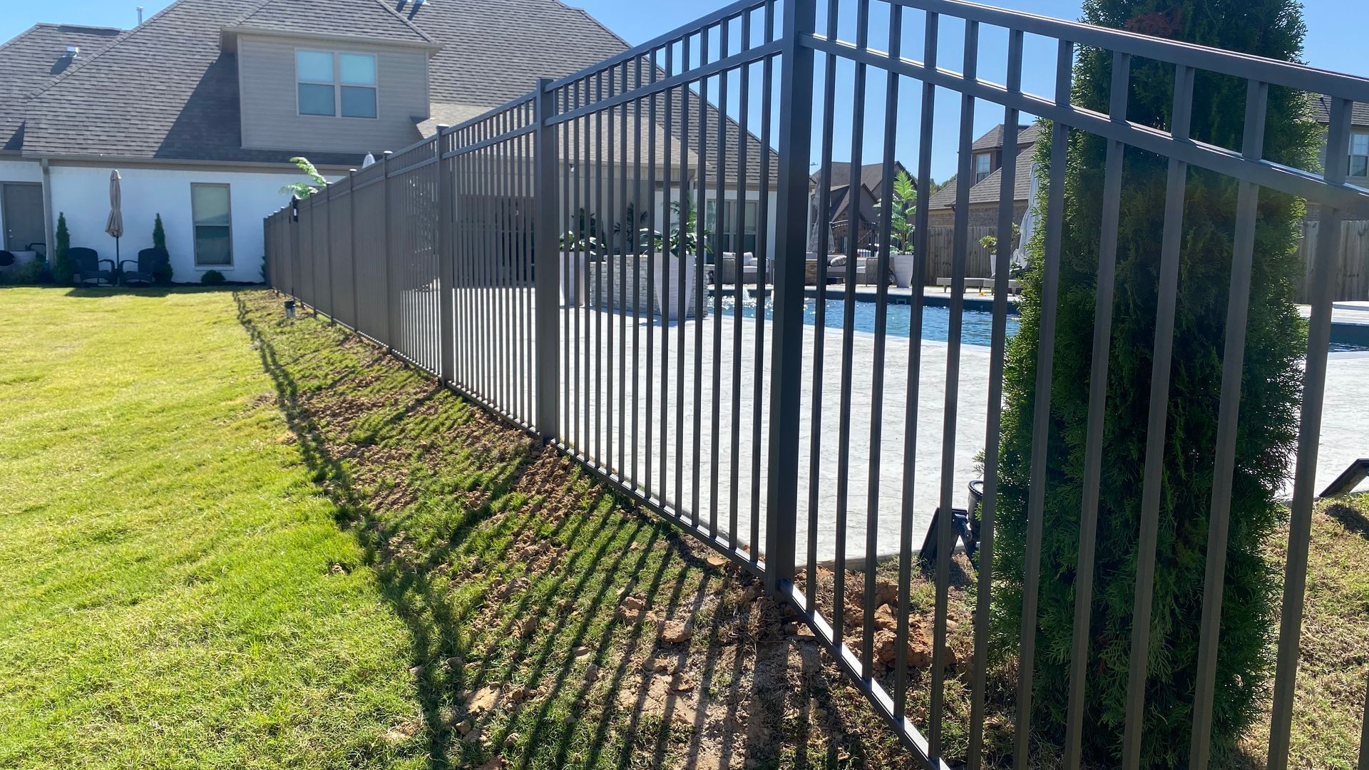 Black metal fence surrounding a swimming pool in a grassy backyard.