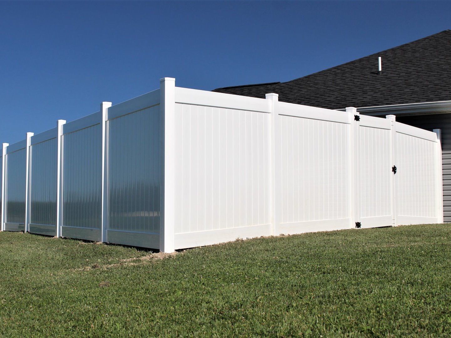 A white fence surrounds a grassy yard in front of a house.