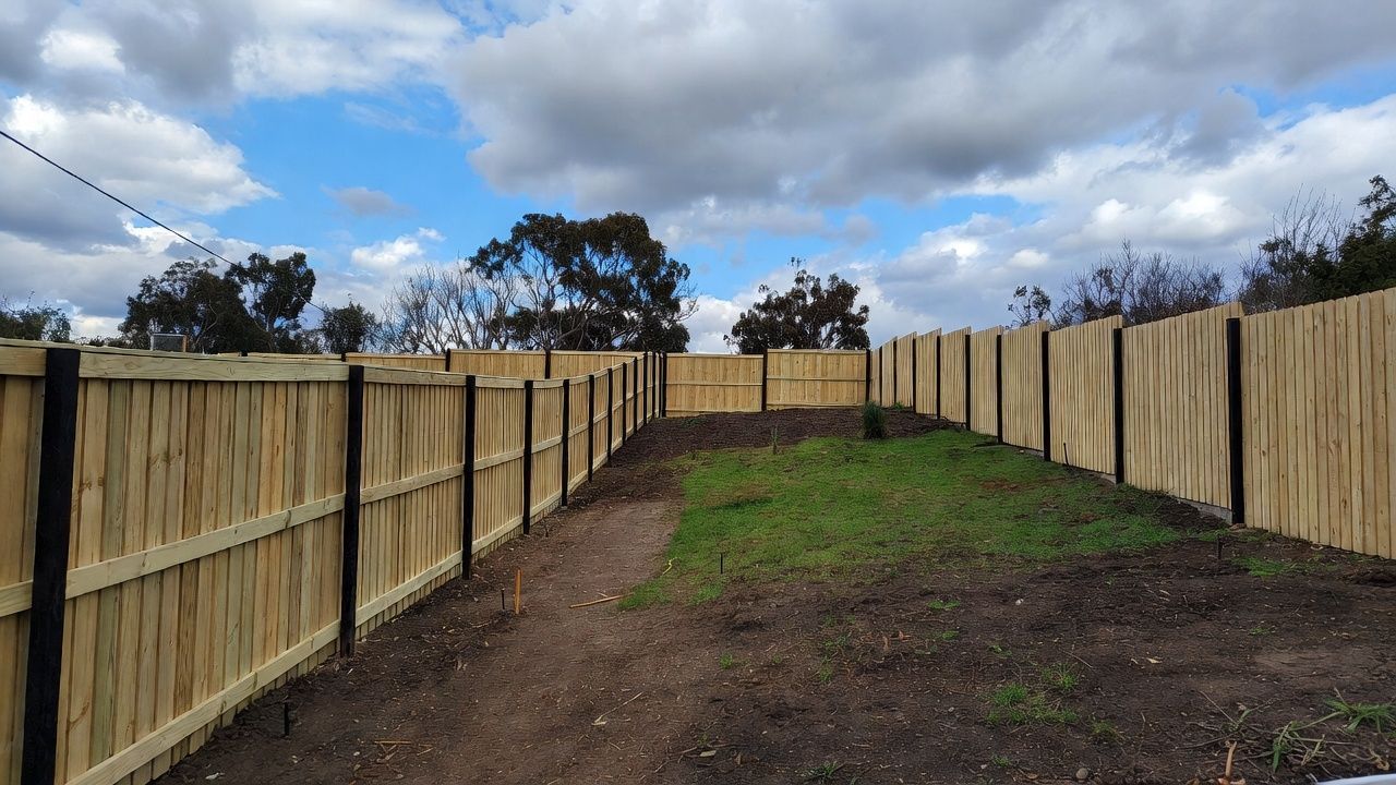 Wooden fence surrounds a grassy backyard, cloudy sky overhead.