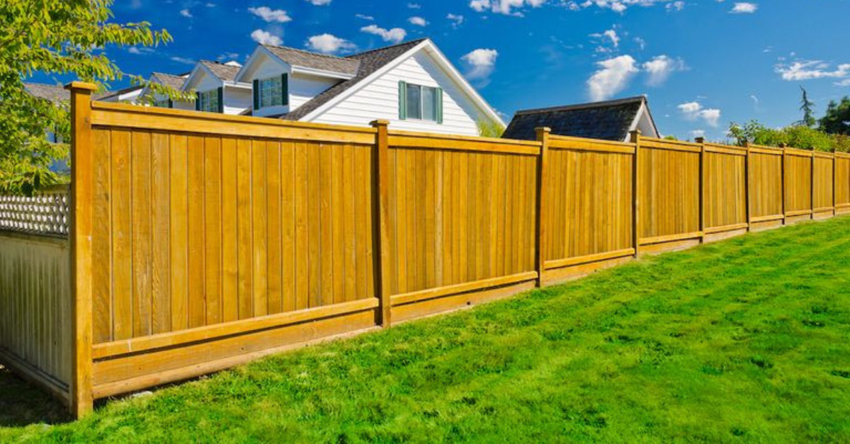 Wooden fence in front of a white house with a green lawn and a blue sky.