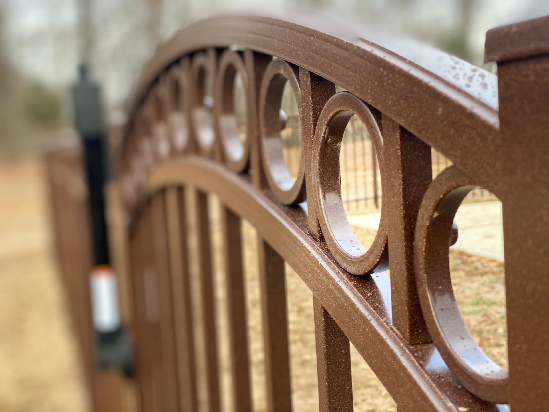 A close up of a wrought iron gate with a fence in the background.